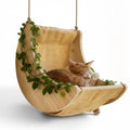 Balançoire Esprit Chat en bois naturel avec hamac en toile beige et chat roux endormi, décorée de feuilles vertes