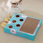 Boîte de jeu interactive pour chat Esprit Chat en carton avec griffoir et balles rouges, design bleu et rose.