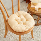 Coussin rond en laine d'agneau beige Esprit Chat posé sur une chaise en bois dans un intérieur chaleureux