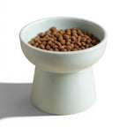 Gamelle surélevée pour chat Esprit Chat en céramique bleu clair remplie de croquettes sur fond beige