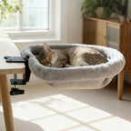 Hamac pour chat Esprit Chat en fausse fourrure grise, fixé au bord d'un bureau en bois avec un chat qui dort dedans.