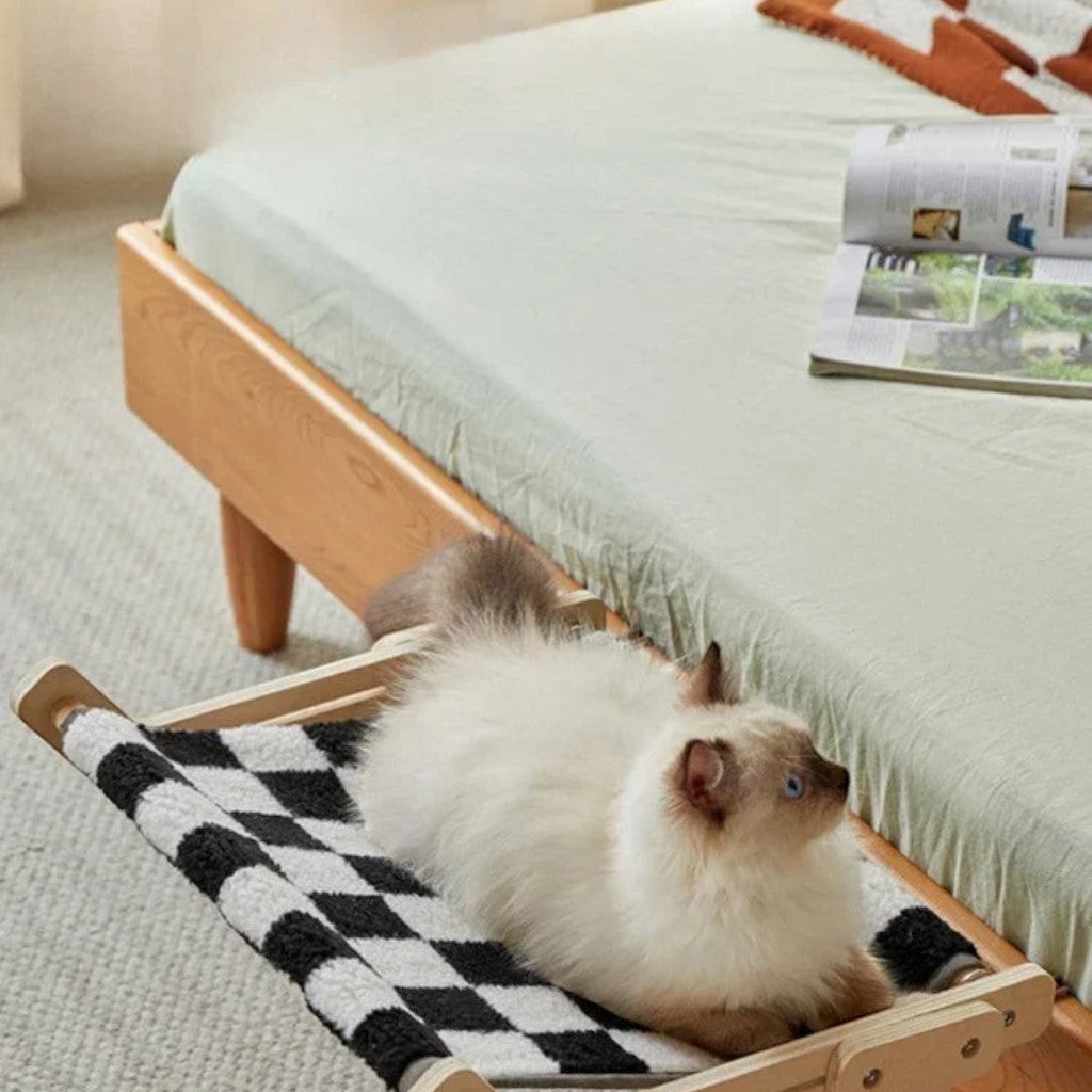 Hamac pour chat Esprit Chat en bois avec tissu à motif damier noir et blanc, installé au pied d'un lit