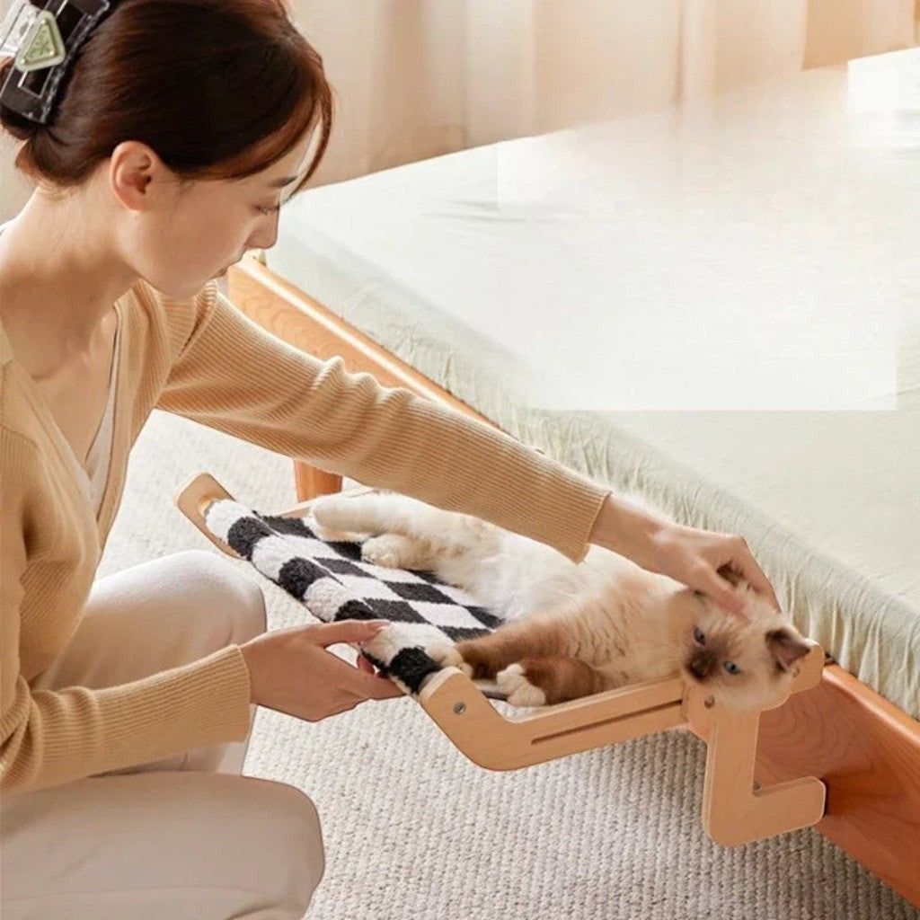Hamac pour chat Esprit Chat en bois avec tissu à carreaux noir et blanc fixé au bord d'un lit