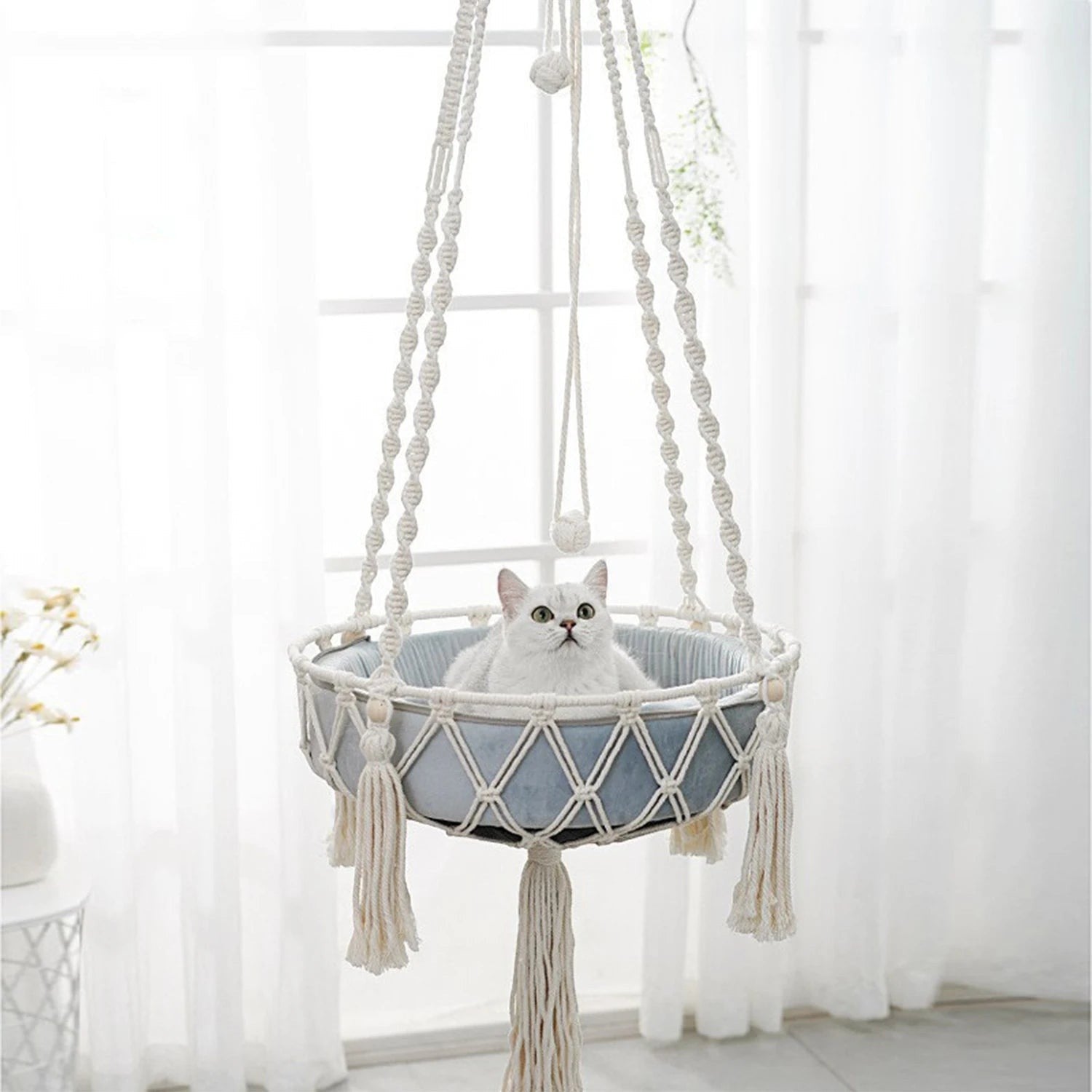 Hamac suspendu Esprit Chat en macramé blanc avec coussin bleu pour chat, style bohème chic et artisanal.