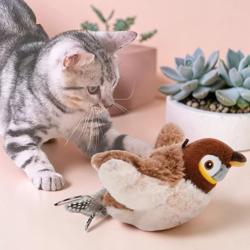 Chat gris jouant avec un oiseau en peluche interactif Esprit Chat sur fond pastel avec des plantes succulentes.