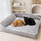 Lit douillet Esprit Chat en velours côtelé gris avec deux chats, un roux et un noir, se reposant confortablement.