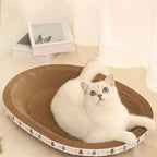 Chat blanc allongé sur un lit griffoir Esprit Chat en carton ondulé beige de forme ovale avec motif de petits chats