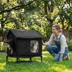 Maison pour chat Esprit Chat sur pieds, imperméable et noire, installée dans un jardin avec une femme souriante.