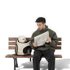 Homme assis sur un banc lisant un journal avec un chien blanc dans un sac de transport Esprit Chat en nylon beige